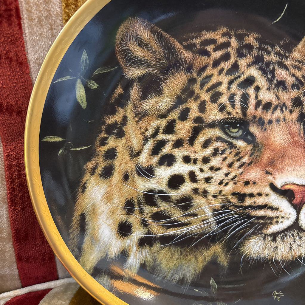 A painted leopard on a black and gold decorative plate sitting on a red and gold striped cushion. 