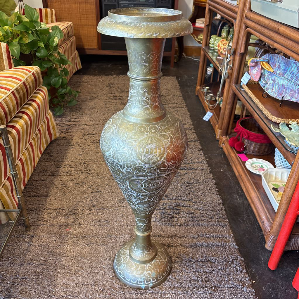 A large, engraved brass vase on a rug in a room setting. 