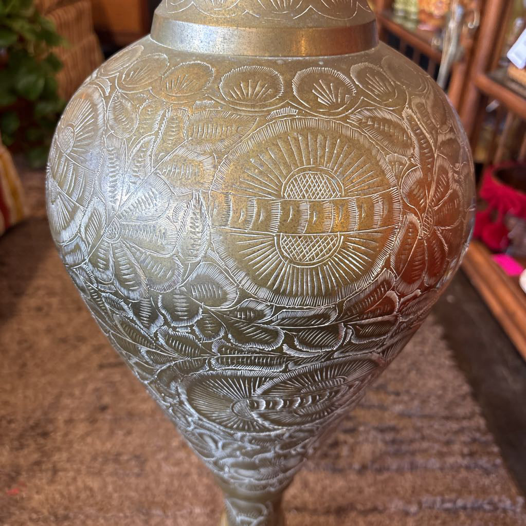 A large, engraved brass vase on a rug in a room setting. 