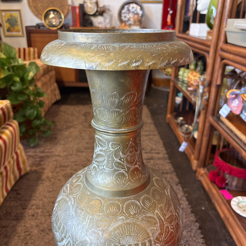 A large, engraved brass vase on a rug in a room setting. 