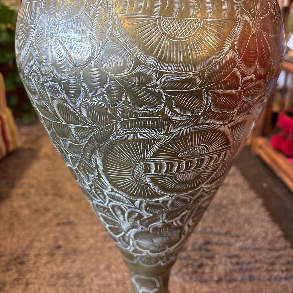 A large, engraved brass vase on a rug in a room setting. 