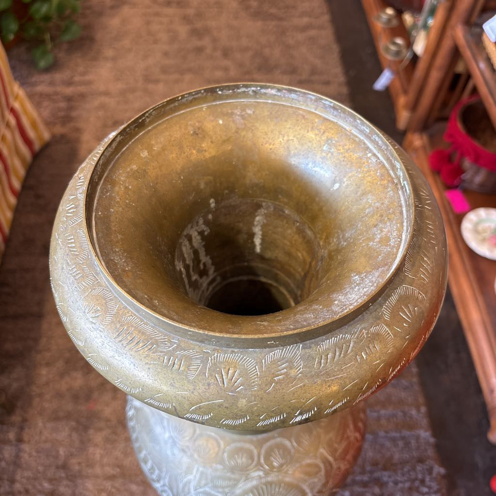 A large, engraved brass vase on a rug in a room setting. 