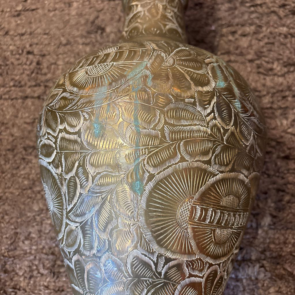 A large, engraved brass vase on a rug in a room setting. 