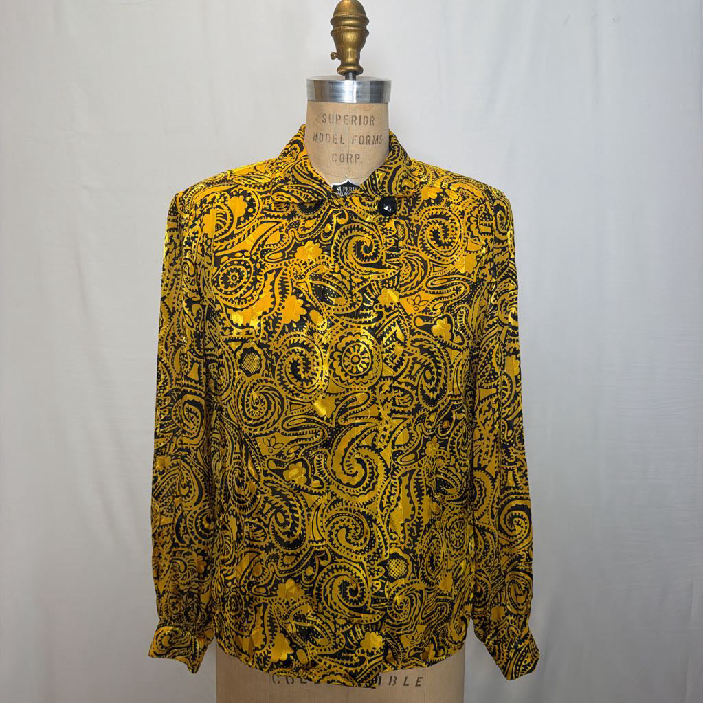 A yellow and black paisley patterned blouse on a mannequin in front of a white wall. 