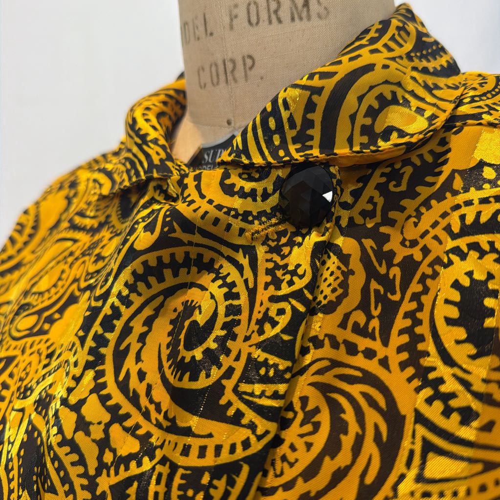 A yellow and black paisley patterned blouse on a mannequin in front of a white wall. 