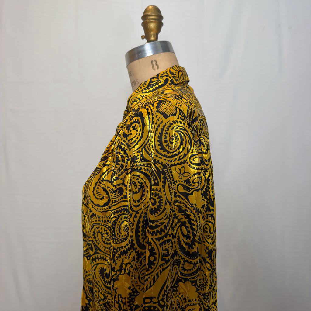 A yellow and black paisley patterned blouse on a mannequin in front of a white wall. 