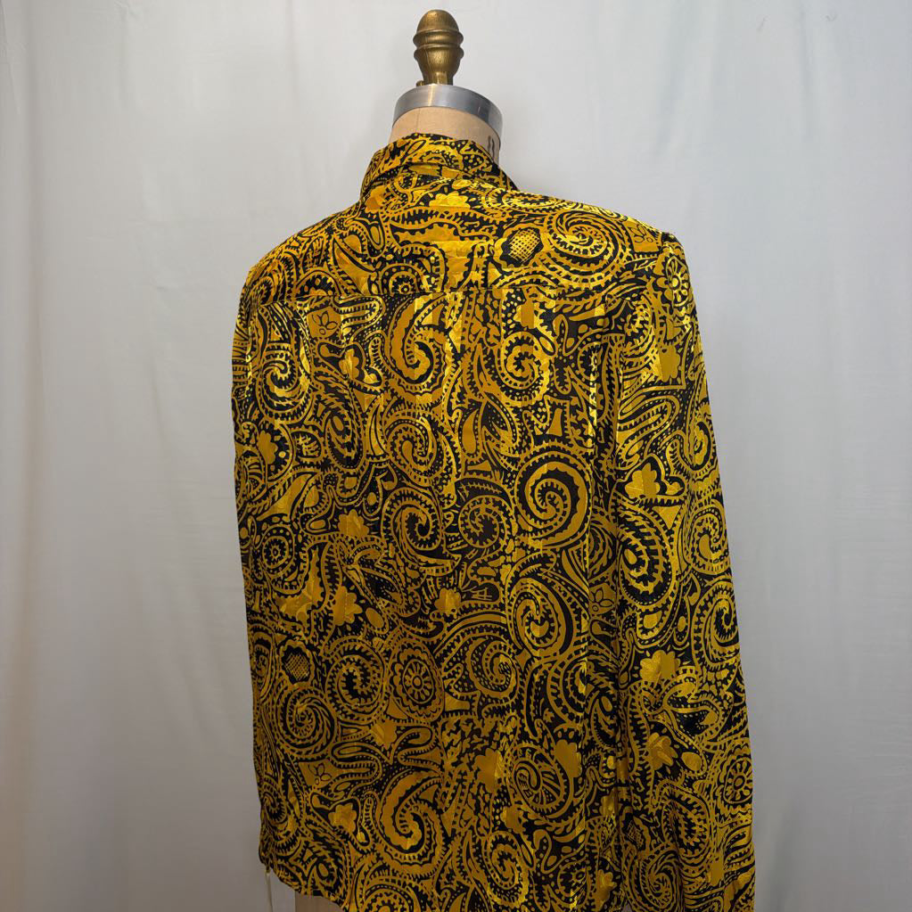 A yellow and black paisley patterned blouse on a mannequin in front of a white wall. 