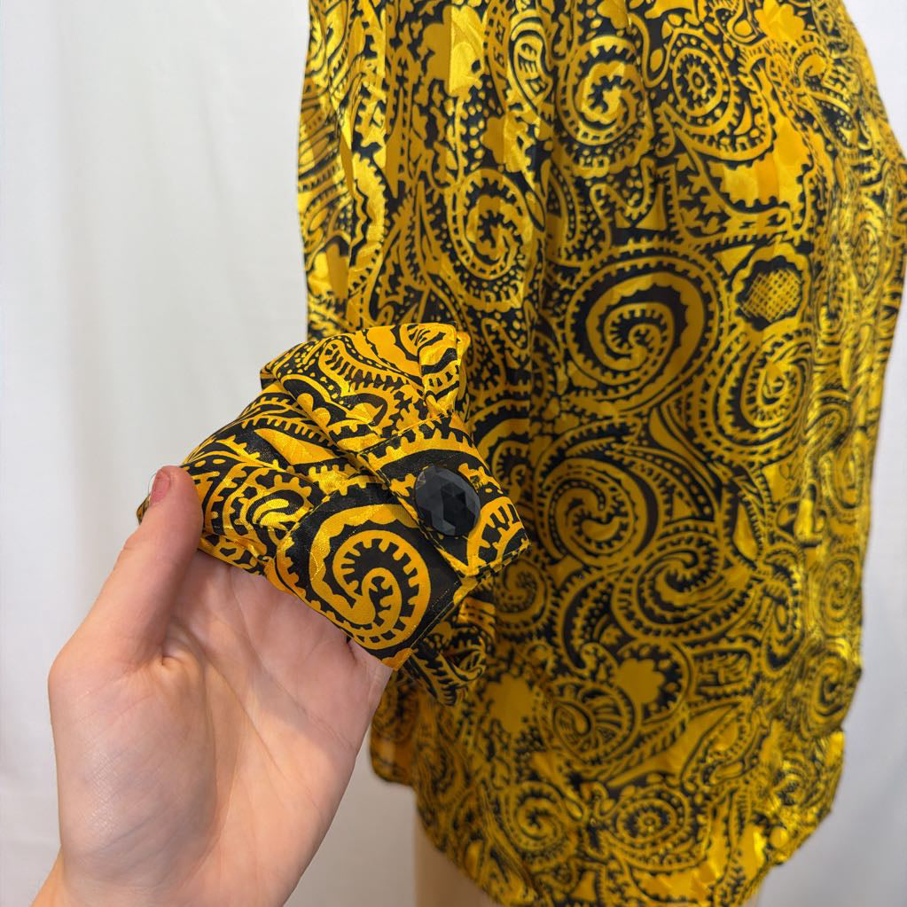 A yellow and black paisley patterned blouse on a mannequin in front of a white wall. 
