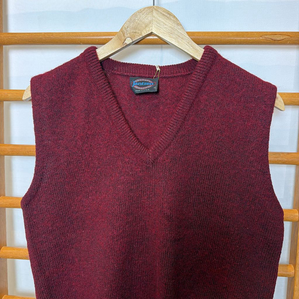 A maroon sweater vest on a wooden rack.