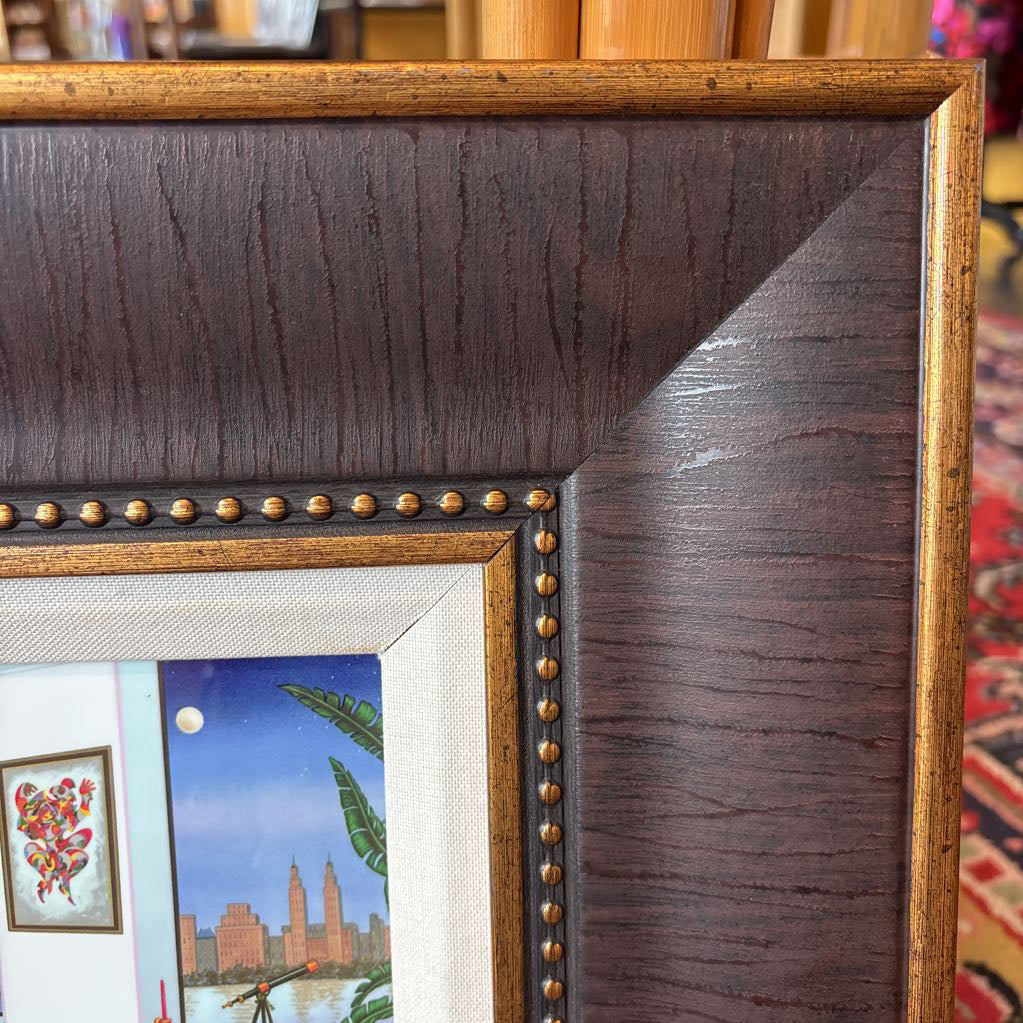 A framed artwork of a room and a nigh time cityscape outside of the windows. 