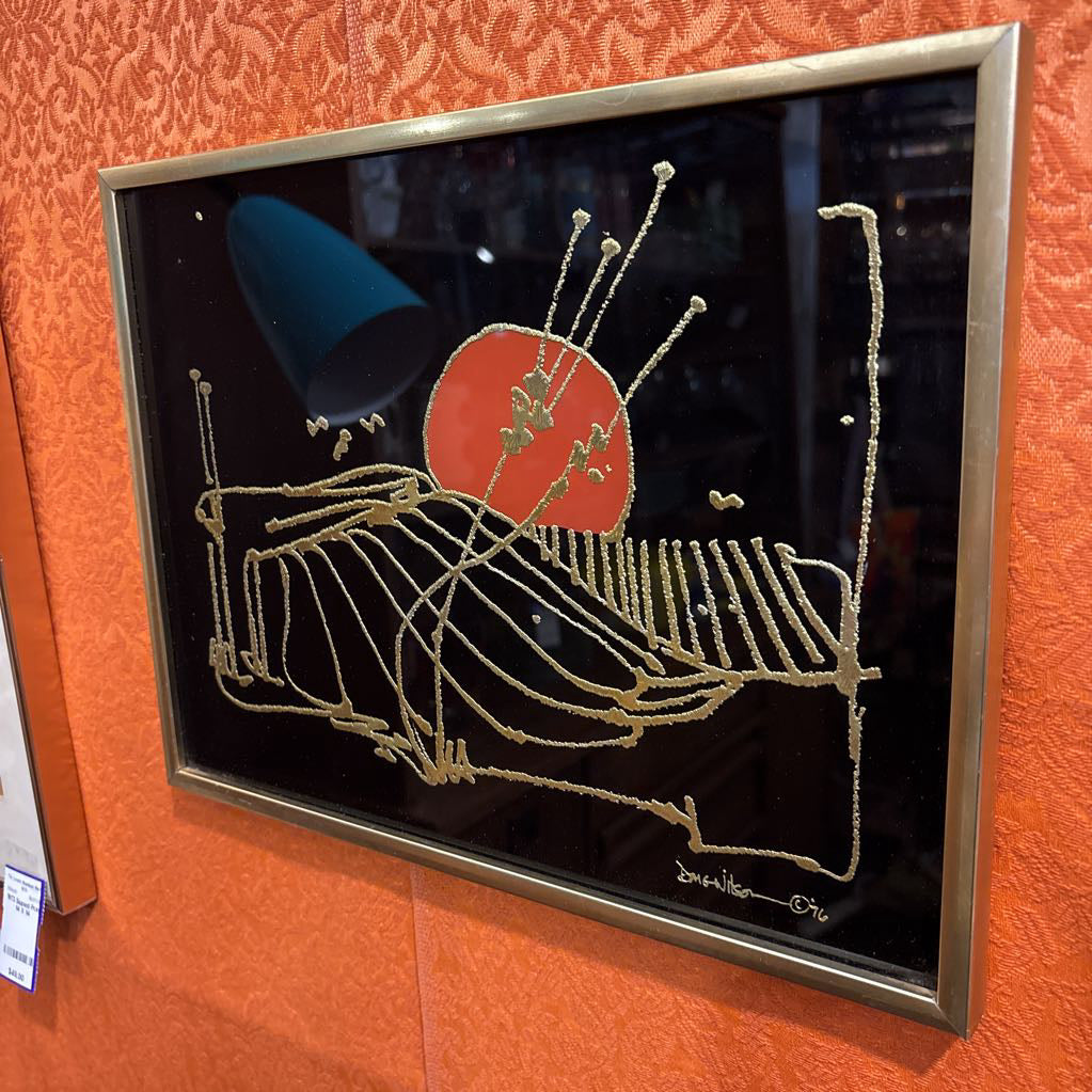A black glossy artwork with textured gold linework and an orange circle. This piece is hanging on an orange fabric overed wall. 