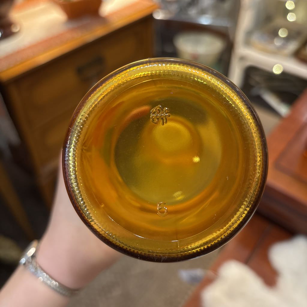 An amber glassware set with a decanter and 5 cordial glasses all with a floral pattern on the front sitting on a wooden table in a store setting. 