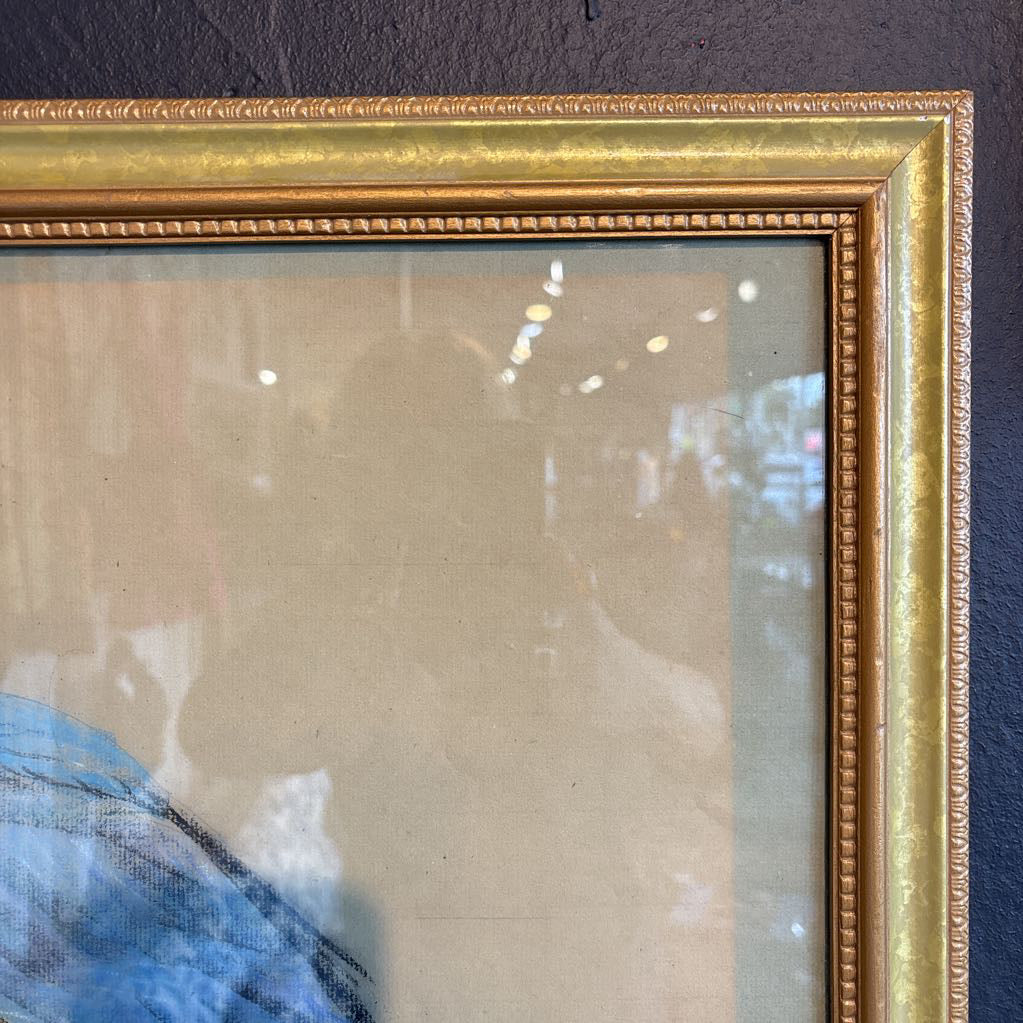 A vintage looking framed artwork of a blue and yellow Macaw on a branch with a signature under it. Its hanging on a black wall. 